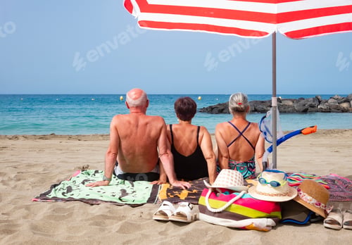 Preview: Rear view of three people friends enjoying together holidays at the beach sitting on the sand