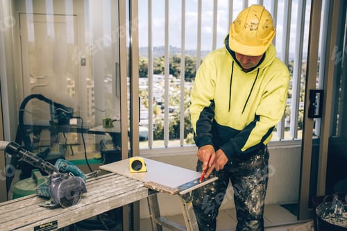 Preview: Man marking marks with pencil on a tile to be cut. Laying ceramic floor tiles, home renovation