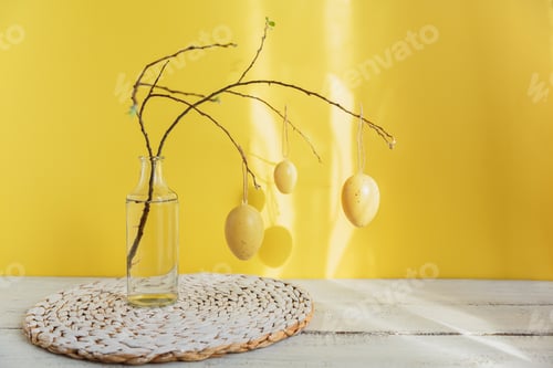 Preview: Easter eggs hanging on branch of spring tree on yellow background with sunlight