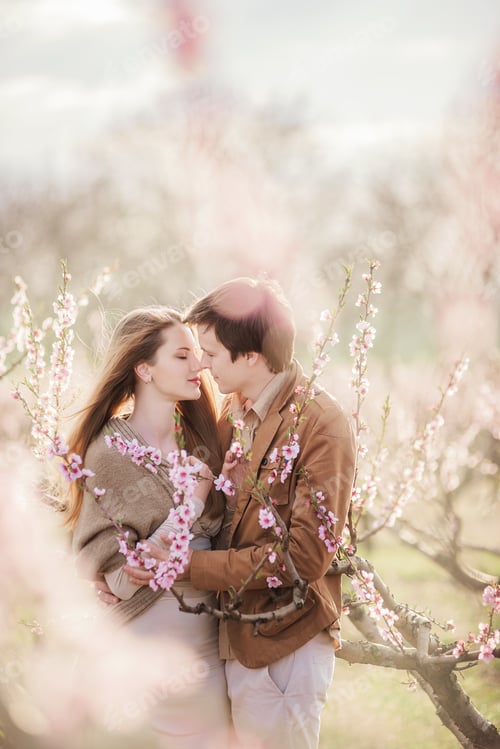 Preview: Happy couple at sunset in blooming peach gardens. Man stands in front of young woman, hugs, kisses