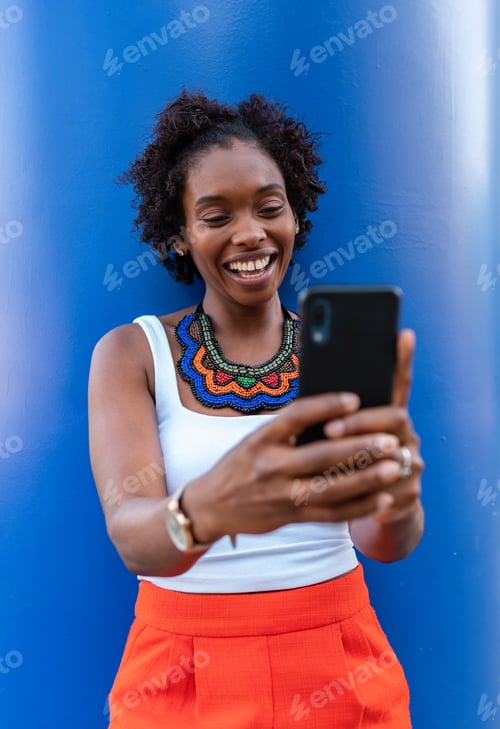 Preview: Joyful black woman using smartphone and walking on street