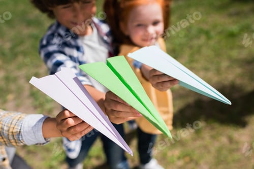 Preview: close-up view of cute little children holding paper planes in park