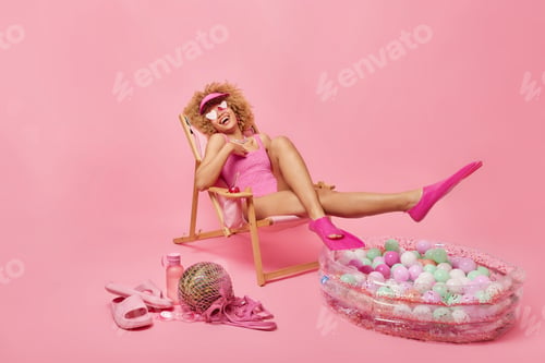 Preview: Overjoyed woman has fun and laughs joyfully wears bathing suit and slippers foolishes around at beac