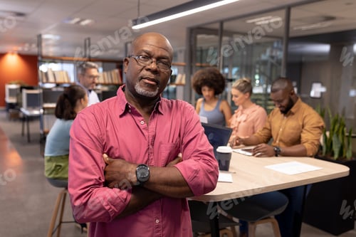 Preview: Portrait of confident mature african american businessman with arms crossed against colleagues