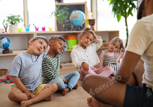 Preview: Nursery school children with man teacher sitting on floor indoors in classroom, doing exercise.