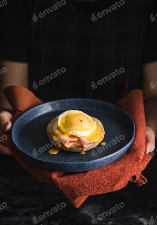 Preview: egg Benedict with hollandaise sauce on dark blue plate on table in kitchen