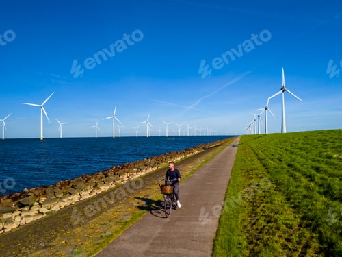 Preview: A man gracefully rides a bike down a picturesque path next to windmill turbines in Spring