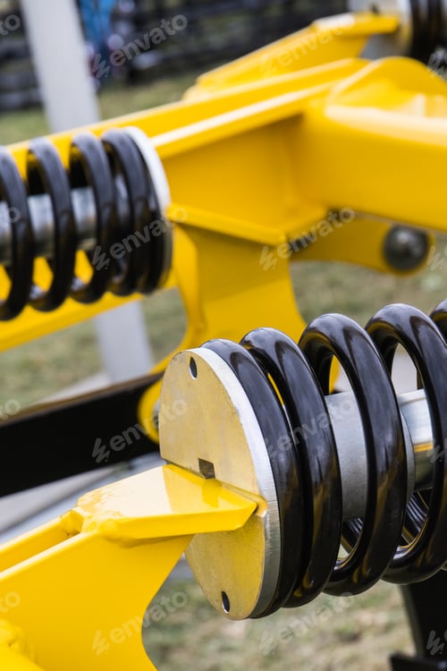 Preview: Steel black spring as part of yellow agricultural machine. Technology