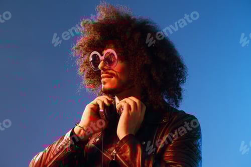 Preview: Portrait of a stylish man with curly hair with glasses and headphones on a blue background