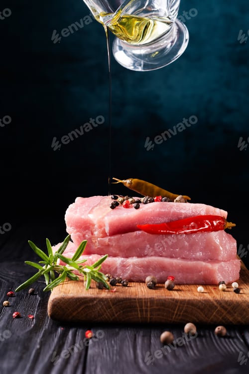 Preview: Stack of steaks of fresh raw pork meat decorated with chili peppers and rosemary with chef's action