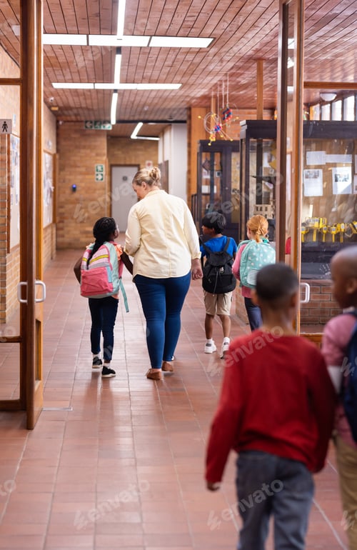 Preview: Walking in school hallway, female teacher guiding young diverse students with backpacks