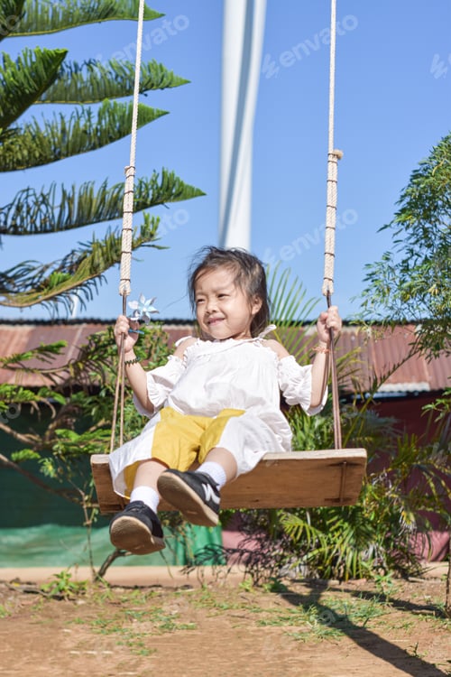 Preview: Little girl is swing at playground in summer garden on warm and sunny day outdoors.