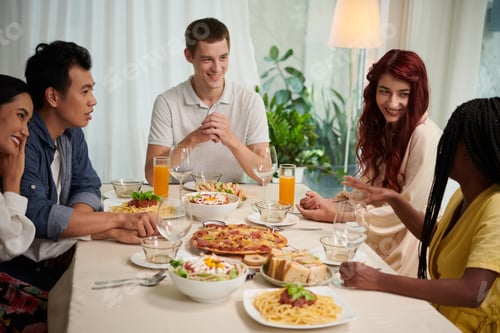 Preview: Group of young intercultural people in smart casualwear chatting by served table