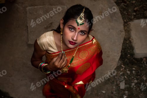 Preview: Young Indian woman in a red saree standing in a dark surrounding looking up