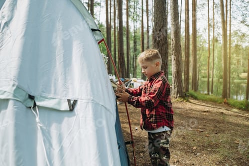 Preview: cute little caucasian boy putting up a tent. Family camping concept