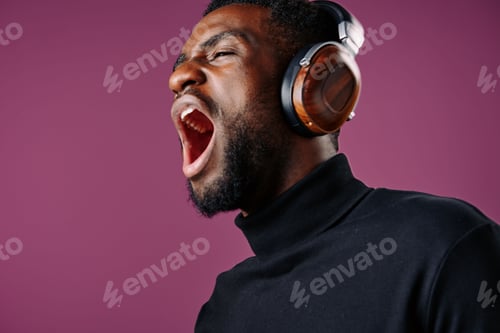 Preview: Young Black man passionately singing with headphones on a vibrant purple background, showcasing