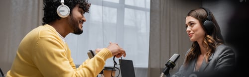 Preview: side view of bearded indian man in yellow jumper and brunette radio host in headphones looking
