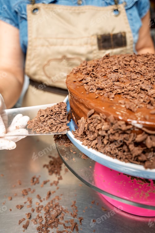 Visualização: Chef de pastelaria decorando bolo de chocolate com raspas de chocolate na cozinha