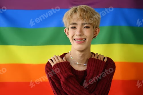 Preview: Cheerful homosexual young gay man posing over rainbow pride flag background.