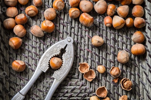 Preview: Closeup hazelnuts with nutcracker and nutshells in old basket