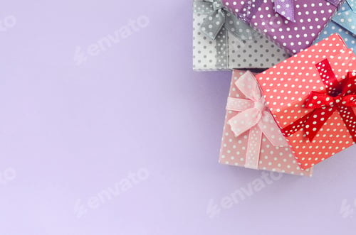 Preview: Pile of a small colored gift boxes with ribbons lies on a violet background