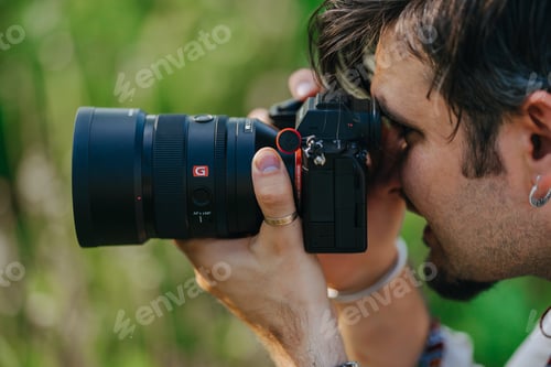 Preview: Man photographer taking photos on professional Sony digital camera with G master lens outdoors.