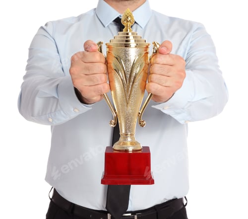 Preview: Young businessman holding gold trophy cup on white background, closeup