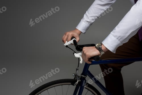 Preview: Partial view of businessman riding on bicycle isolated on grey