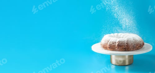 Preview: Icing sugar falling on bundt cake, blue background