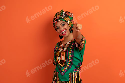 Preview: Positive cute black lady in african costume pointing at camera