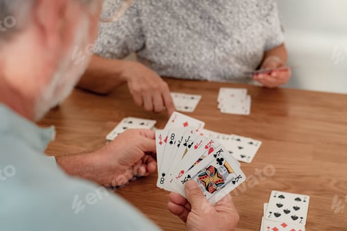 Preview: Closeup on senior couple at home in competition playing with cards on a wooden table
