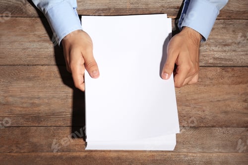 Preview: Man holding blank paper sheets for brochure at wooden table, top view. Mock up