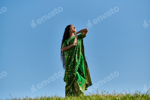 Aperçu: summer enjoyment, green field, indian woman in ethnic wear smiling with closed eyes under blue sky