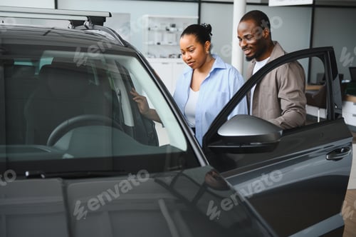 Preview: Couple examining new car in dealership showroom