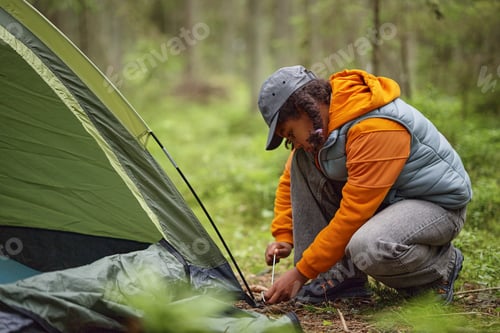 Preview: Young Black Woman Assembling Tent While Camping Outdoors in Forest Setting