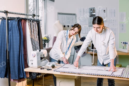 Preview: Waist up portrait of two young beautiful women tailors working with clothing