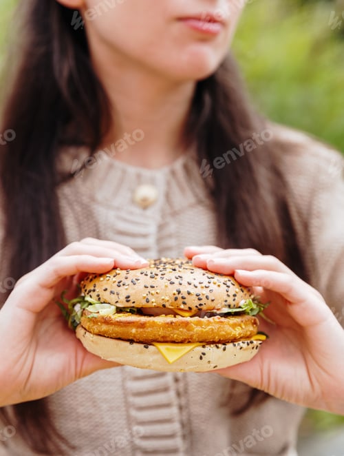 Preview: A young girl holds a delicious burger with both hands.