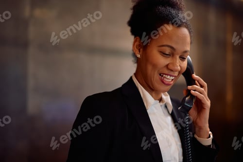 Preview: Happy black hotel manager talking on the phone at reception desk.
