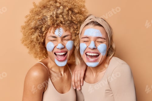 Preview: Overjoyed positive young women stand closely to each other keep mouthes opened apply beauty mask for