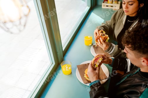 Preview: Couple eating burgers and drinking orange juice at restaurant window