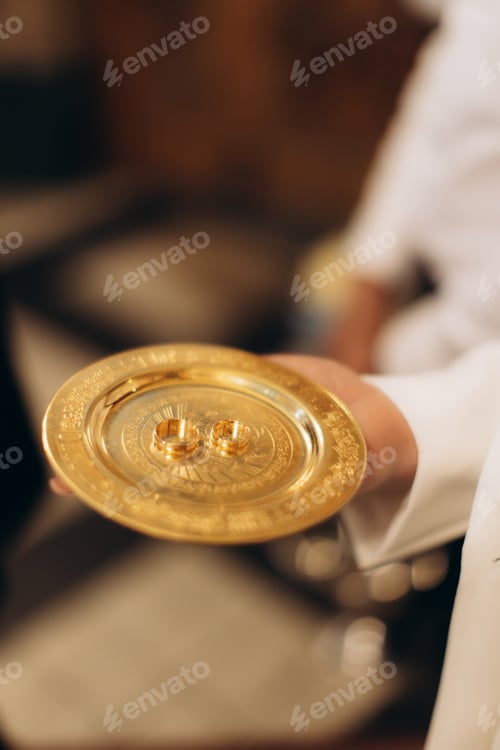 Preview: Priest holding wedding rings on golden plate for ceremony