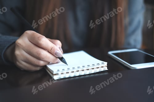 Preview: a woman's hands writing on notebook with mobile phone on the table