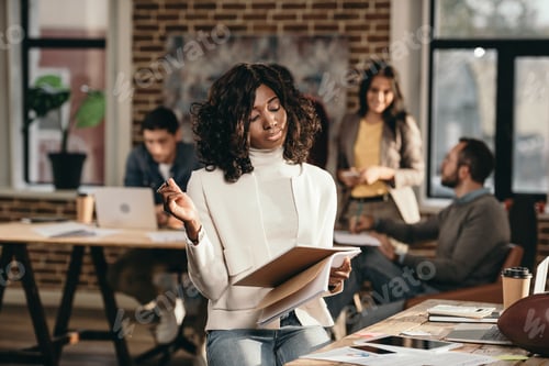 Preview: focused african american casual businesswoman holding journal with colleagues working behind in loft