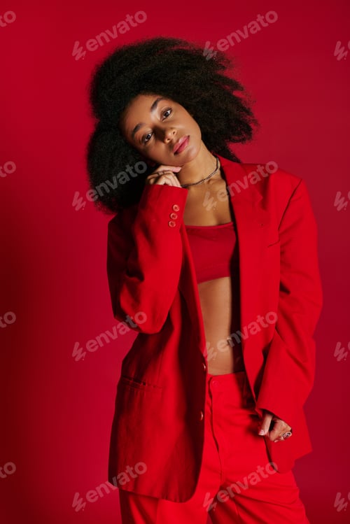 Preview: appealing alluring african american woman in vibrant attire looking at camera on red backdrop