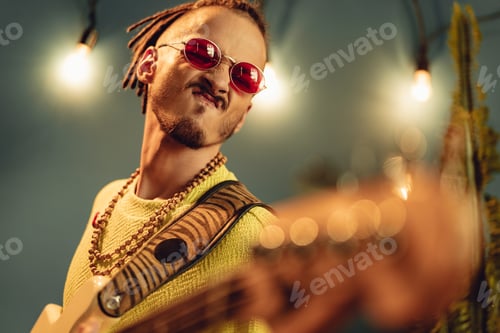 Preview: Young fashionable man in pink sunglasses playing guitar with joy