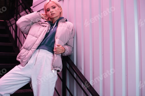 Preview: blonde young woman in down jacket looking at camera on stairs