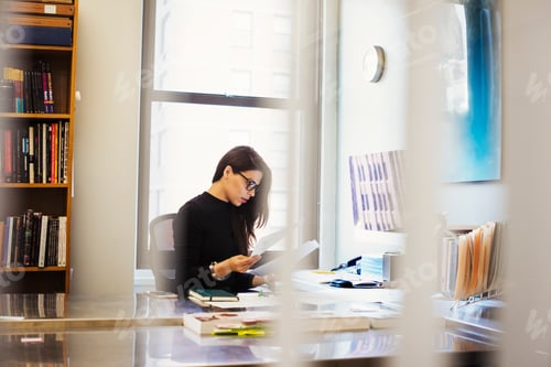 Preview: A young woman sitting at a desk in an office looking at paperwork.