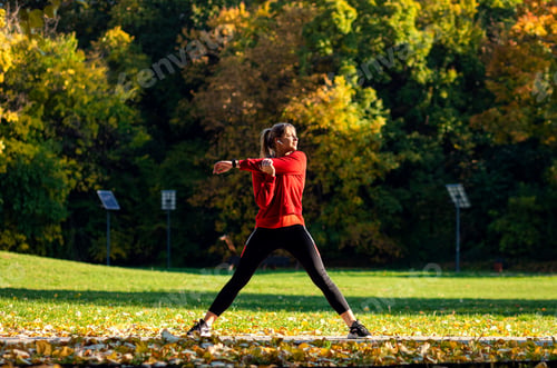 Preview: Young woman warming up and stretching before running in park.