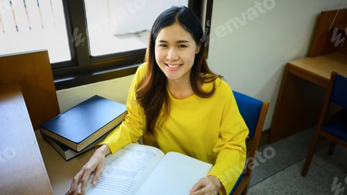 Preview: Beautiful asian female student reading book, doing class assignment. in library.