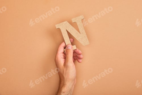 Preview: partial view of man holding paper cut letter N on beige background